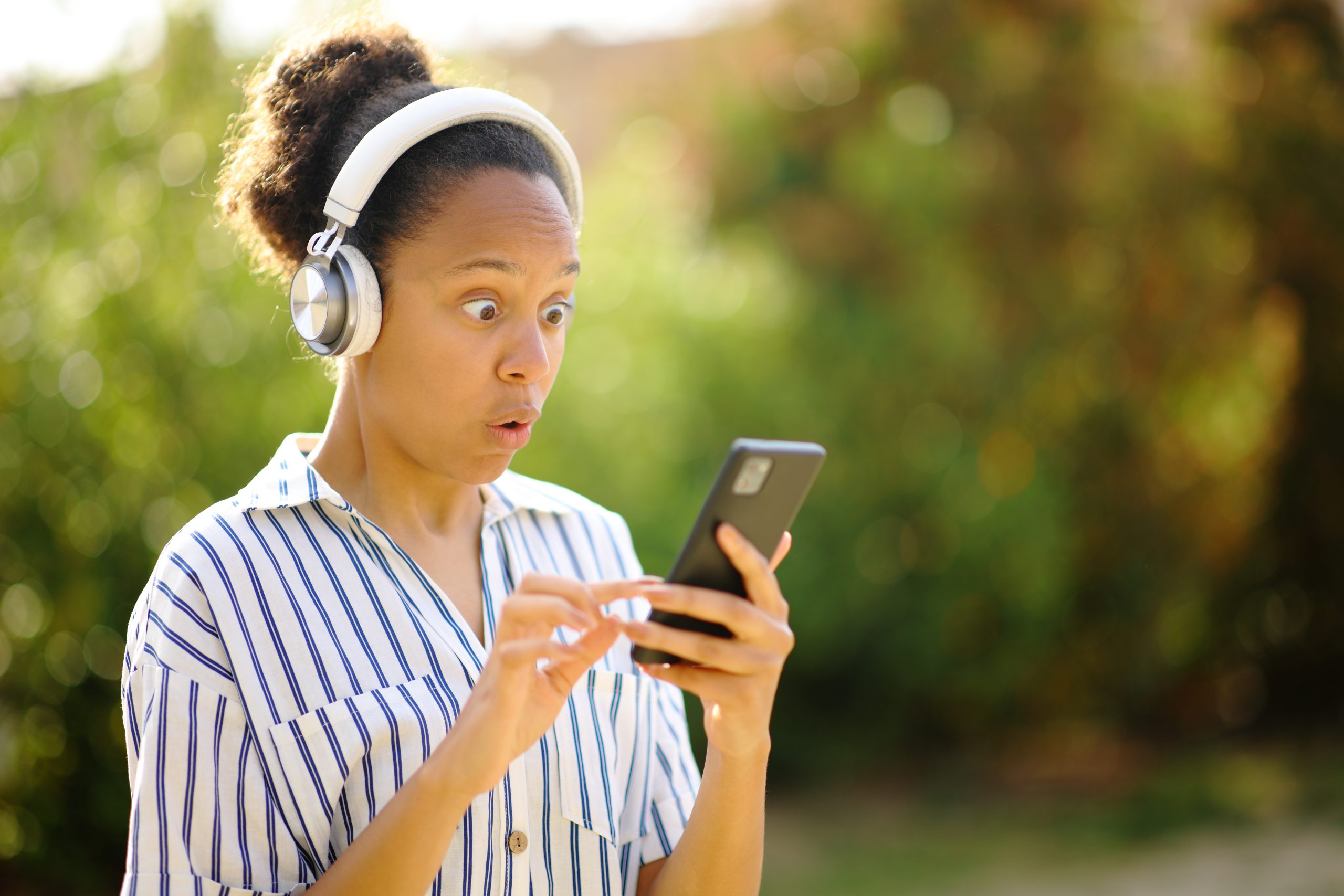 Surprised black woman listening to music on phone