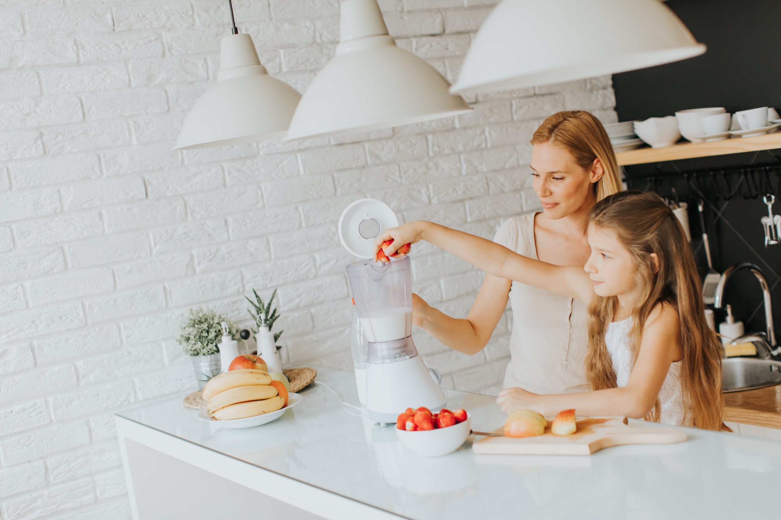Mother and daughter preparing shealthy smoothie in the modern kitchen