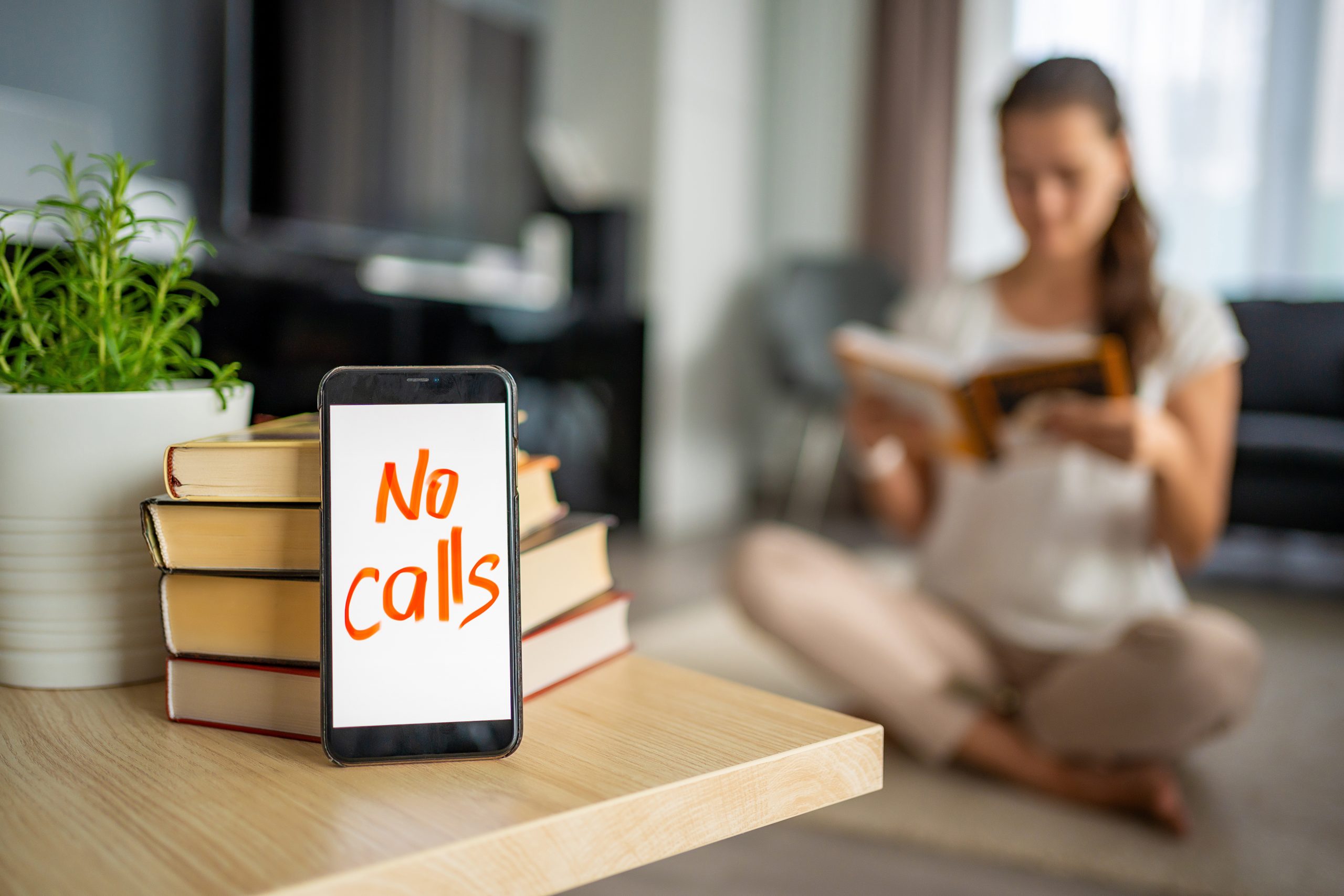 Digital detox concept photo. Smartphone with text No Calls and woman reading book in background. High quality photo